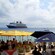 People in the ocean and sitting in chairs around tables under umbrellas on the beach with a Disney Cruise Line ship in the distance